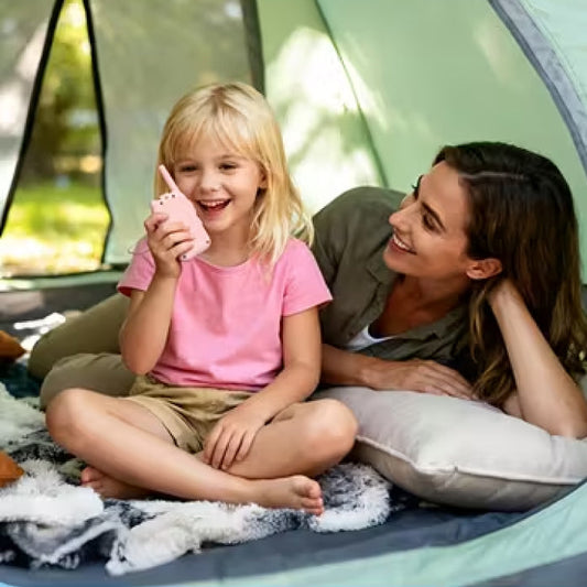 A smiling girl talking into a pink walkie-talkie in a tent